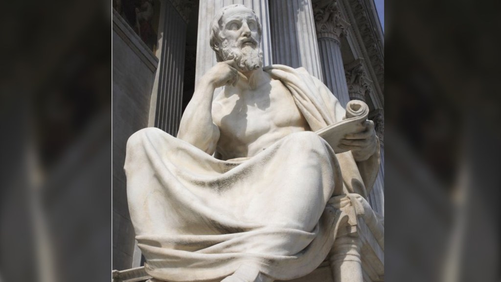 A marble statue of Herodotus, depicted with a thoughtful expression, holding a scroll. The statue is placed against a decorative building backdrop, showcasing columns and classical architecture.